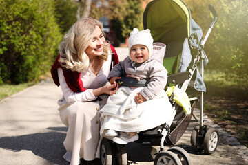 Naklejka premium Happy mother with her daughter in stroller outdoors on sunny day