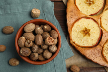 Nutmeg seeds and tasty apple pie on wooden table, flat lay