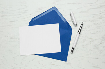 Envelope with blank paper card and pen on white wooden table, flat lay