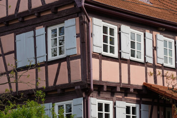 Eckansicht von einem historisches Fachwerkhaus. Das alte Gebäude ist rot verputzt und besticht durch seine vielen Sprossenfenster, die alle mit Holzläden ausgestattet sind.
