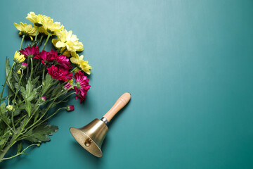 Golden school bell and bouquet of beautiful chrysanthemum flowers on green chalkboard, flat lay....