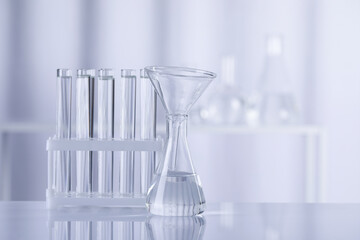 Different laboratory glassware with transparent liquid on table against blurred background. Space for text