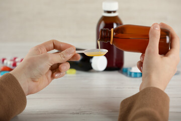 Woman pouring cough syrup into spoon at white wooden table, closeup