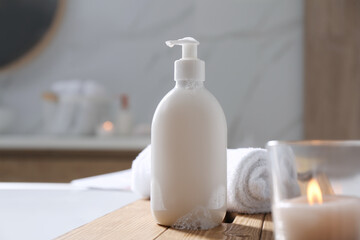 Fototapeta na wymiar Wooden bath tray with shower gel, candle and fresh towel on tub indoors