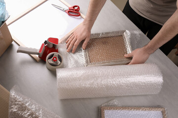 Man covering photo frame with bubble wrap at light grey table, closeup - obrazy, fototapety, plakaty