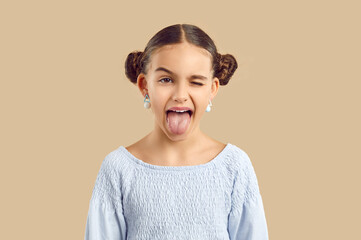 Happy child sticking tongue out. Studio shot of a cheerful naughty kid making a funny grimace. Pretty little girl with adorable space hair buns and modern earrings shows her tongue and winks her eye - Powered by Adobe
