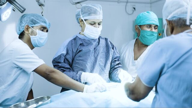 woman surgeon busy stitching skin after surgery at operation theatre - concept of surgical suture, treatment and teamwork
