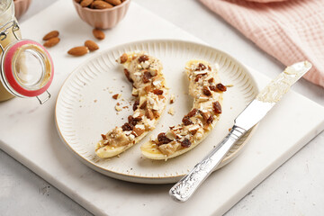 Two banana halves ready with peanut butter topping, raisins, almonds and chia seeds on white plate on marble board