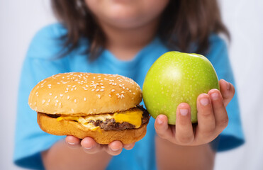 The child holds an apple and a burger