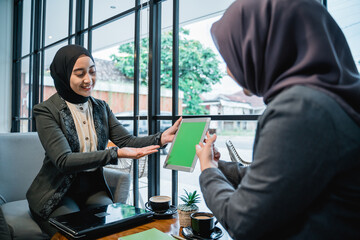 beautiful muslim female worker discussing with her colleague using tablet