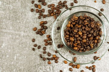 Transparent cup of coffee with coffee beans on gray concrete background with scattering of coffee beans. Arabica, Robusta. Drink for office, home. Top view, flat lay, mockup with copy space for text