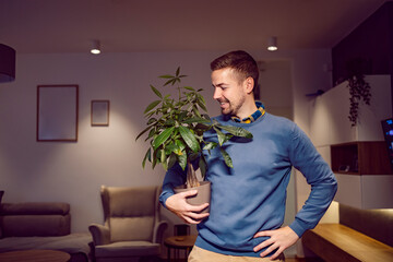 A man standing at home with houseplant.