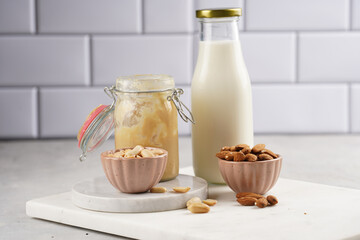 Peanuts, almonds in pink bowls, homemade peanut butter and almond milk on marble boards. Vegan food