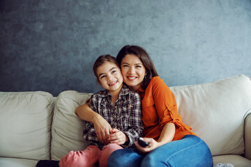 Smiling mother and daughter sitting on the sofa, hugging and watching television.