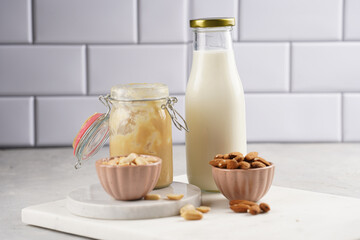 Peanuts, almonds in pink bowls, homemade peanut butter and almond milk on marble boards. Vegan food