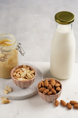 Peanuts, almonds in pink bowls, homemade peanut butter and almond milk on marble boards. Close-up on nuts