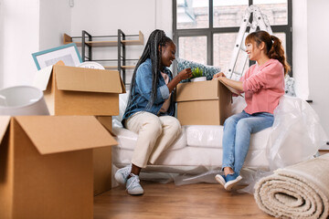 moving, people and real estate concept - happy smiling women unpacking boxes at new home