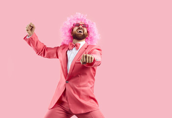 Cheerful crazy man in pink wig making funny dance moves isolated on pink background. Eccentric man in pink formal suit rejoices, has fun and dances in gangnam style. Banner. - obrazy, fototapety, plakaty