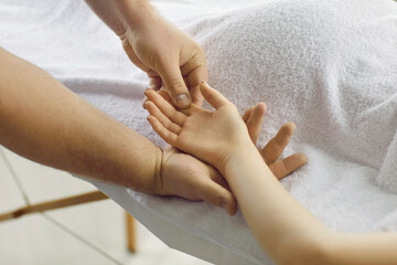Male masseur doing relaxing hand massage to young woman lying on massage table in spa. Close up of male therapist hands massaging female palms and fingers. Concept of massage spa treatments.