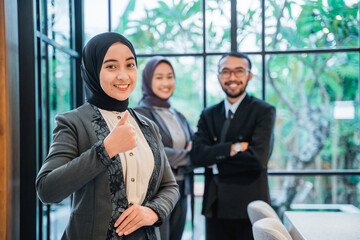 business muslim woman showing thumb up to camera with partner at the background smiling