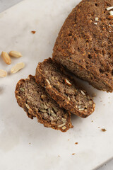 Homemade gluten-free and yeast-free buckwheat whole bread bread loaf with sunflower and pumkin seeds and nuts, cut in slices on white marble board
