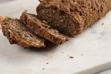 Homemade gluten-free and yeast-free buckwheat whole bread bread loaf with sunflower and pumkin seeds and nuts, cut in slices on white marble board
