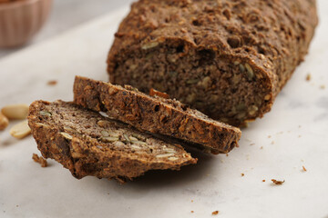 Homemade gluten-free and yeast-free buckwheat whole bread bread loaf with sunflower and pumkin seeds and nuts, cut in slices on white marble board