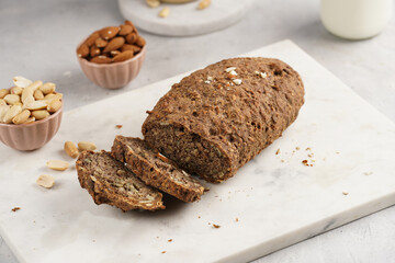 Homemade gluten-free and yeast-free buckwheat whole bread bread loaf with sunflower and pumkin seeds and nuts, cut in slices on white marble board