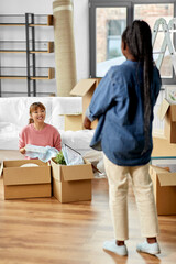 Fototapeta na wymiar moving, people and real estate concept - women unpacking boxes at new home