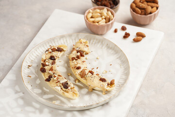 Two banana halves ready with peanut butter topping, raisins, almonds and chia seeds on white plate...