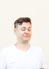 Wet young caucasian man in white t-shirt with closed eyes and water is flowing from his face....