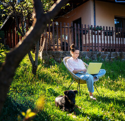 Young beautiful happy smiling woman working in home office outdoors in garden, using laptop.