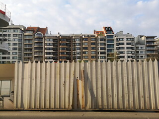 Bauzaun in Beige und Naturfarben vor modernen Apartmenthäusern im Licht der Abendsonne in...