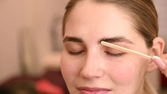 Permanent eyebrow styling. The master applies the composition for laminating the eyebrows with a wooden spatula. 