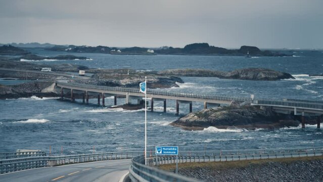 Iconic Atlantic ocean road winding through the archipelago. Powerful waves crash on the rocks and bridge support columns. Seagulls fly low above the water. Slow-motion.