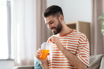 drinks and people concept - smiling man drinking orange juice with straw at home