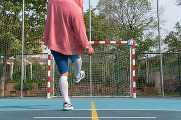 Obraz premium Male in front of a soccer ball shooting at goal. Close-up image of a person who has just kicked a white, red and blue ball in front of a soccer goal on a blue court with yellow lines.
