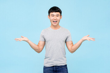 Positive smiling Asian man in causal wear with opening hands standing on light blue isolated...