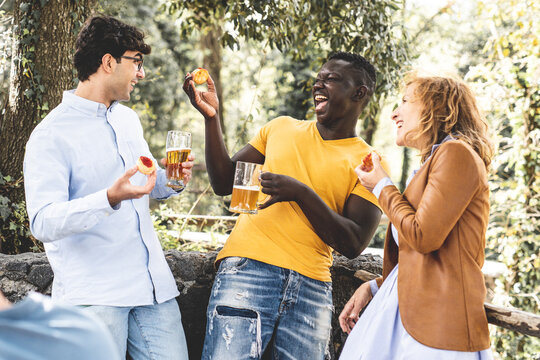 multiracial group of friends laughing and having fun at party, mixed age range group celebrating something eating snack and drinking beers