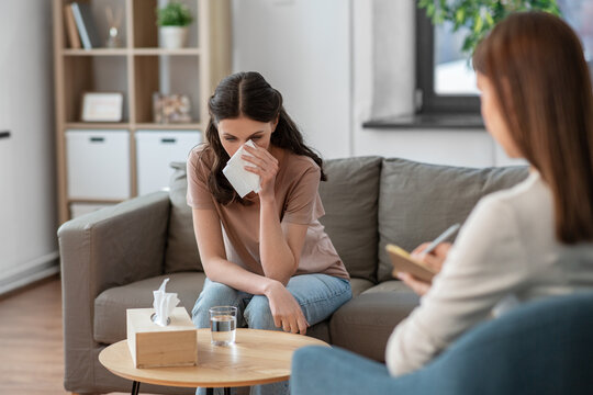 psychology, mental health and people concept - crying woman patient wiping tears with paper tissue and psychologist at psychotherapy session