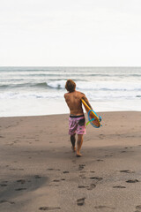A surfer man walks with a board on a sandy beach. Handsome young man on the beach. water sports. Healthy active lifestyle. Surfing. Summer vacation. Extreme sport.