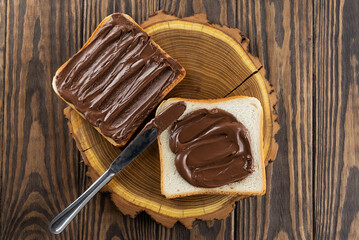 Slices of toast bread with chocolate hazelnut spread with a knife on a wooden table. Top view, flat lay.