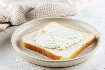 A slice of toast bread with cream cheese in a plate on the table.
