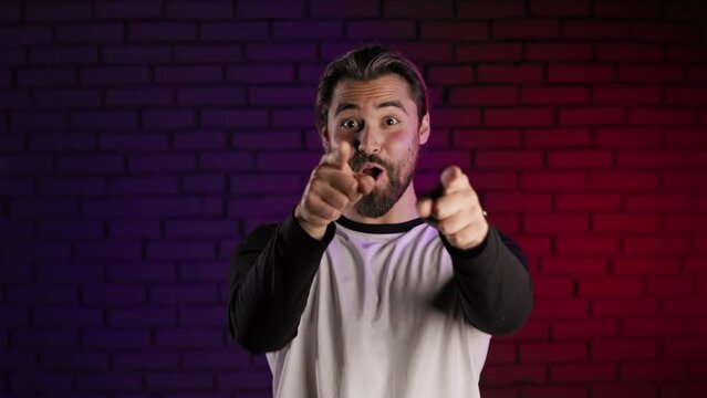 Portrait of positive good looking man in casual clothes smiling on camera and pointing with fingers in studio. Handsome male person advicing or choosing something.