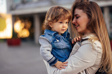 Fototapeta premium Side profile of a beautiful young mother, holding her male toddler, outdoor.