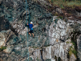 Photo of an adult male, using a rope as a help, climbing on the rock.