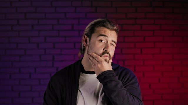 Portrait of handsome man touching his trendy beard with haircut and gesturing thumb up on camera while standing in studio. Satisfaction with appearance and narcissism concept.