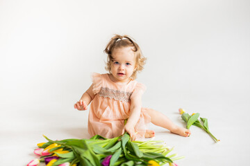 portrait of a little blonde girl with a bouquet of spring flowers on a light background. a child in a pink dress holds a bouquet of tulips in his hands. place for text. spring and summer concept. 