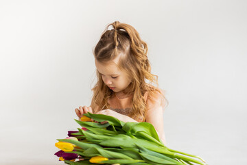 portrait of a little blonde girl with a bouquet of spring flowers on a light background. a child in a pink dress holds a bouquet of tulips in his hands. place for text. 