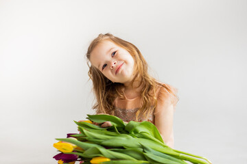 portrait of a little blonde girl with a bouquet of spring flowers on a light background. a child in a pink dress holds a bouquet of tulips in his hands. place for text. 